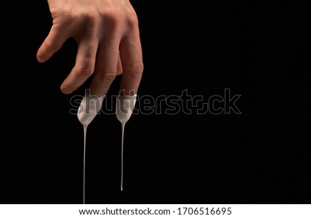 Female hand in liquid white, drops drip from fingers, on a black background. Human hands isolated in a black background.