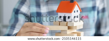 Female hand is listening to wooden blocks on which toy house stands. Unauthorized construction of houses and its consequences concept