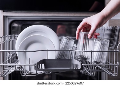 Female hand loading dished, empty out or unloading dishwasher with utensils. Kitchen appliances, lifestyle view. Woman puts a plate in the dishwasher or takes from it. Housewife does her housework  - Shutterstock ID 2250829607