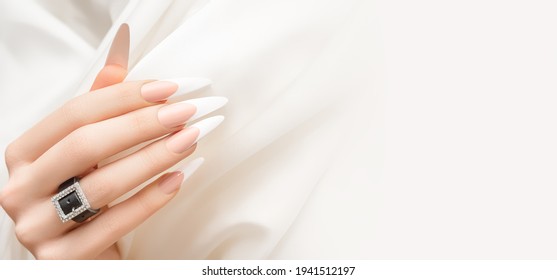 Female hand with long french nail design. Long french nail polish manicure. Woman hand on white fabric background