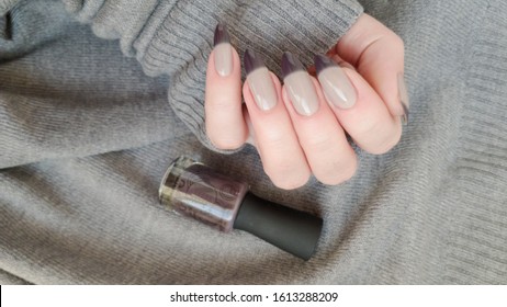 Female hand and long nails   beige brown manicure holds bottle nail polish
