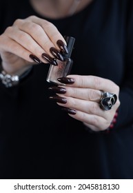 Female hand and long nails   black manicure holds bottle nail polish