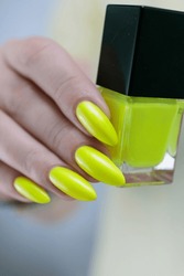 Female Hand With Long Nails And A Bottle Of Bright Yellow Green Neon Nail Polish