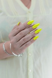 Female Hand With Long Nails And A Bottle Of Bright Yellow Green Neon Nail Polish