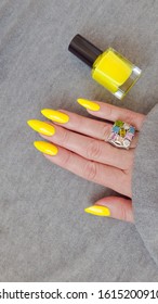 Female Hand With Long Nails And A Bottle Of Bright Yellow Neon Nail Polish