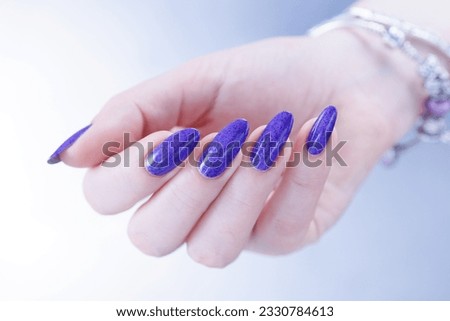 Female hand with long nails and a bottle of light blue lilac color nail polish