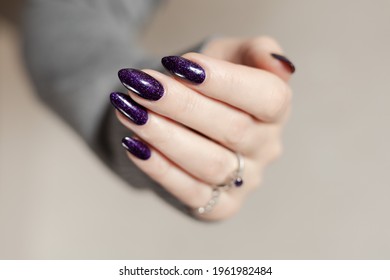 Female hand and long nails   dark purple lilac manicure holds bottle nail polish