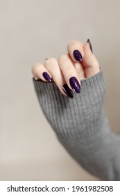 Female hand and long nails   dark purple lilac manicure holds bottle nail polish