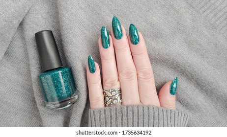 Female hand and long nails   green manicure holds bottle nail polish