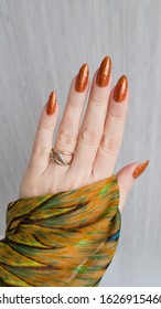 Female hand and long nails   orange ginger manicure holds bottle nail polish