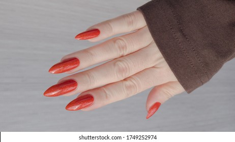 Female hand and long nails   orange ginger manicure holds bottle nail polish