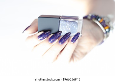 Female hand and long nails   purple lilac manicure holds bottle nail polish