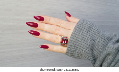 Female hand with long nails and a red manicure holds a bottle of nail polish