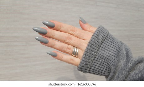 Female hand with long nails and a white gray silver manicure holds a bottle of nail polish