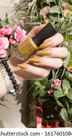 Female hand and long nails   yellow mustard manicure holds bottle nail polish