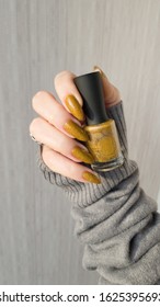 Female hand and long nails   yellow mustard manicure holds bottle nail polish