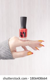 Female hand and long nails   yellow  orange   red gradient manicure holds bottle nail polish