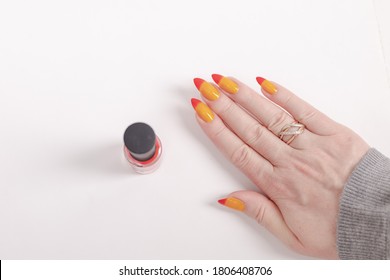 Female hand and long nails   yellow  orange   red gradient manicure holds bottle nail polish