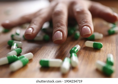 Female Hand Lying On Scattered Capsules Closeup. Drug Overdose Concept