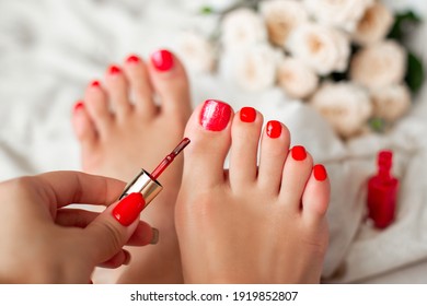 Female Hand Making Pedicure And Applying Red Gel Polish On Nails, Sitting At Bed
