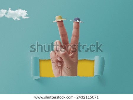Female hand making a V sign and wearing tiny beach hats on two fingers, the hand is coming out from a hole in torn paper, summer vacations concept