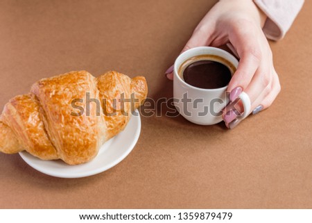Female hand with manicure holding cup of coffee and eating croissant. Breakfast in french style