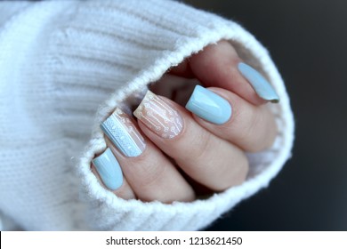 Female hand with manicure light blue and white nail polishes with aztec pattern on the nails