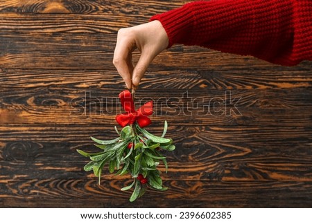 Female hand with mistletoe branch on wooden background