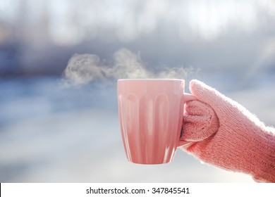 Female hand in mittens holding cup with hot tea or coffee. Tea break. Winter and Christmas time concept
