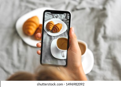 Female hand with mobile phone taking picture of tasty breakfast coffee and croissants in bed, closeup - Powered by Shutterstock