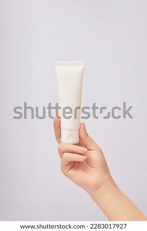 Female hand model holding an empty label white tube over white background. Concept of beauty products cream