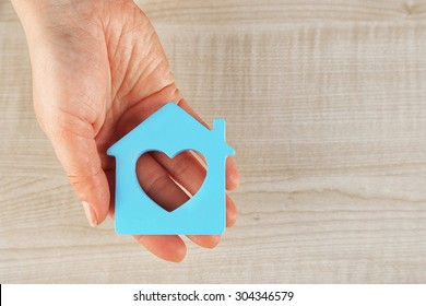 Female hand with model of house on wooden table background
