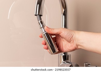 Female hand with modern chrome faucet with remote hose. Kitchen faucet with pull-out spout