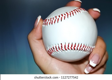 female hand and nails and French manicure holding white baseball and red seam at gradient menthol background