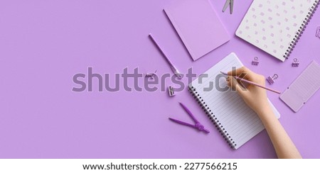 Female hand with notebooks and stationery on lilac background with space for text