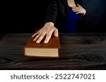 Female hand on the Bible and on the constitution book during the inauguration in parliament or the oath in court. Woman taking Oath of Office. Dark background, blue office clothes