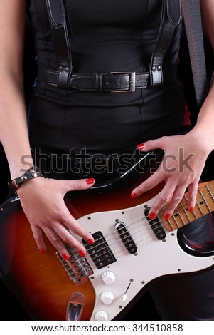female hand on the detail of a guitar in dark back. Rock star 