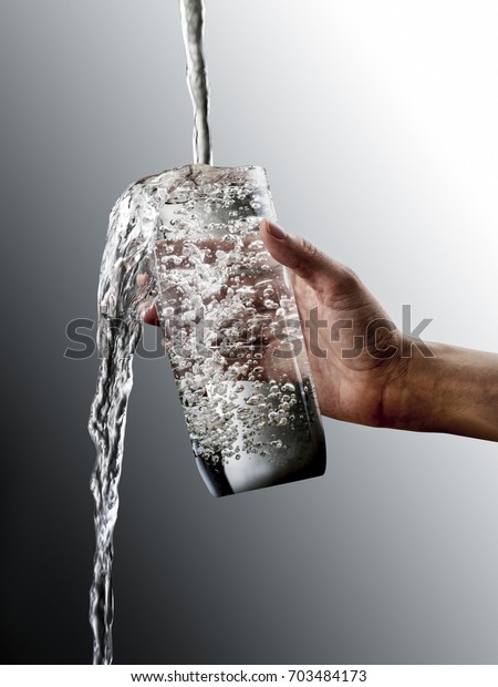 Female hand with overflowing glass of water on
grey gradation