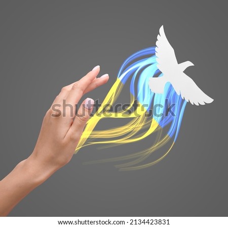 Female hand and paper dove on grey background. Stop the war in Ukraine