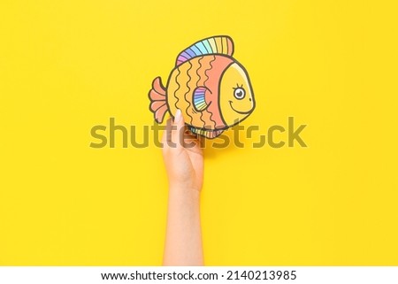 Female hand with paper fish on yellow background. April Fools Day celebration Photo stock © 