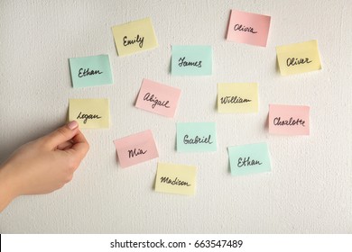Female hand and paper stickers with different names on white wall. Concept of choosing baby name