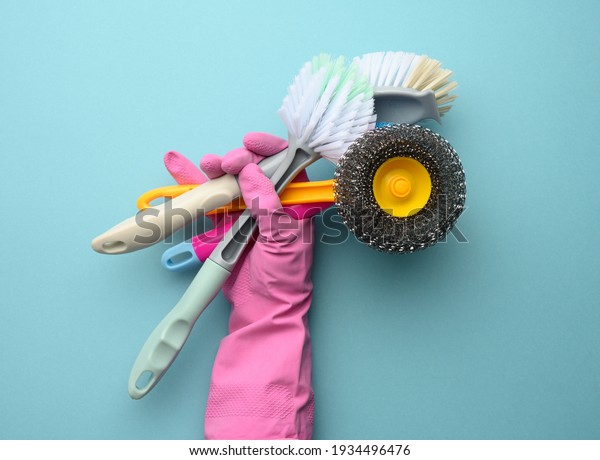 female hand in a pink glove holds a stack\
of plastic cleaning brushes, blue\
background