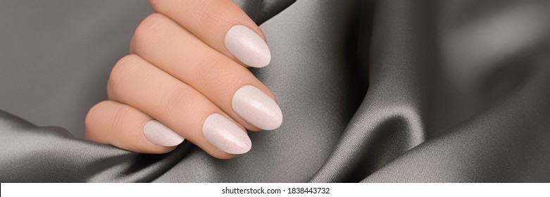 Female hand with pink nail design. Rose glitter nail polish manicure. Woman hand on gray fabric background. Banner