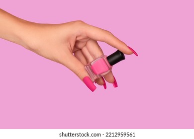 Female hand with pink nail design. Mate pink nail polish manicure. Female model hand with perfect manicure hold pink nail polish bottle on pink background. Copy space. Place for text.