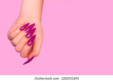 Female hand with pink stiletto nail design. Glitter pink nail polish manicure. Female hand with stiletto nails on red background. Copy space. Plce for text.