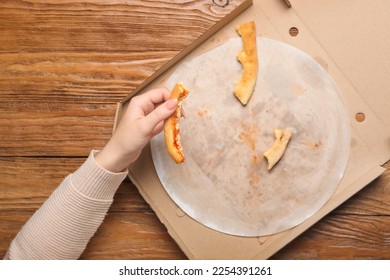 Female hand with pizza leftovers on wooden background - Powered by Shutterstock