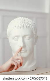 Female hand pokes a finger into the nose of Gypsum sculpture of Caesar's head. Head stands on a wooden table in classic interior - Shutterstock ID 1706037343