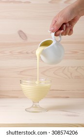 Female Hand Pouring Condensed Milk On A Light Wooden Background