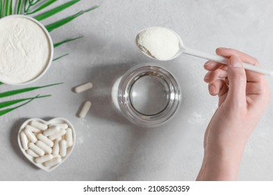 A female hand pours collagen powder or protein into a glass of water on a gray background. Natural beauty and health supplement. Top view, flat lay.