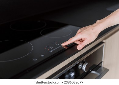 Female hand press button on digital control panel of electric cooker hob. Woman choose temperature for cooking at glass ceramic stove. Concepts of modern domestic appliance in kitchen